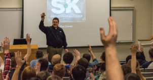 Members of the Society for Automotive Engineers raise their hands in a meeting