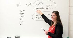 Female teacher pointing and teaching next to whiteboard with Spanish words.