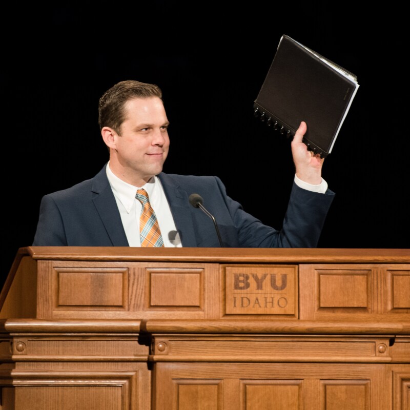 The devotional speaker raises his notebook.