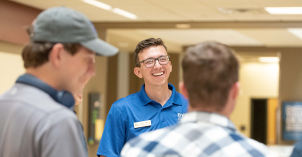 A male peer mentor smiles while greeting several other male BYU-Idaho students.