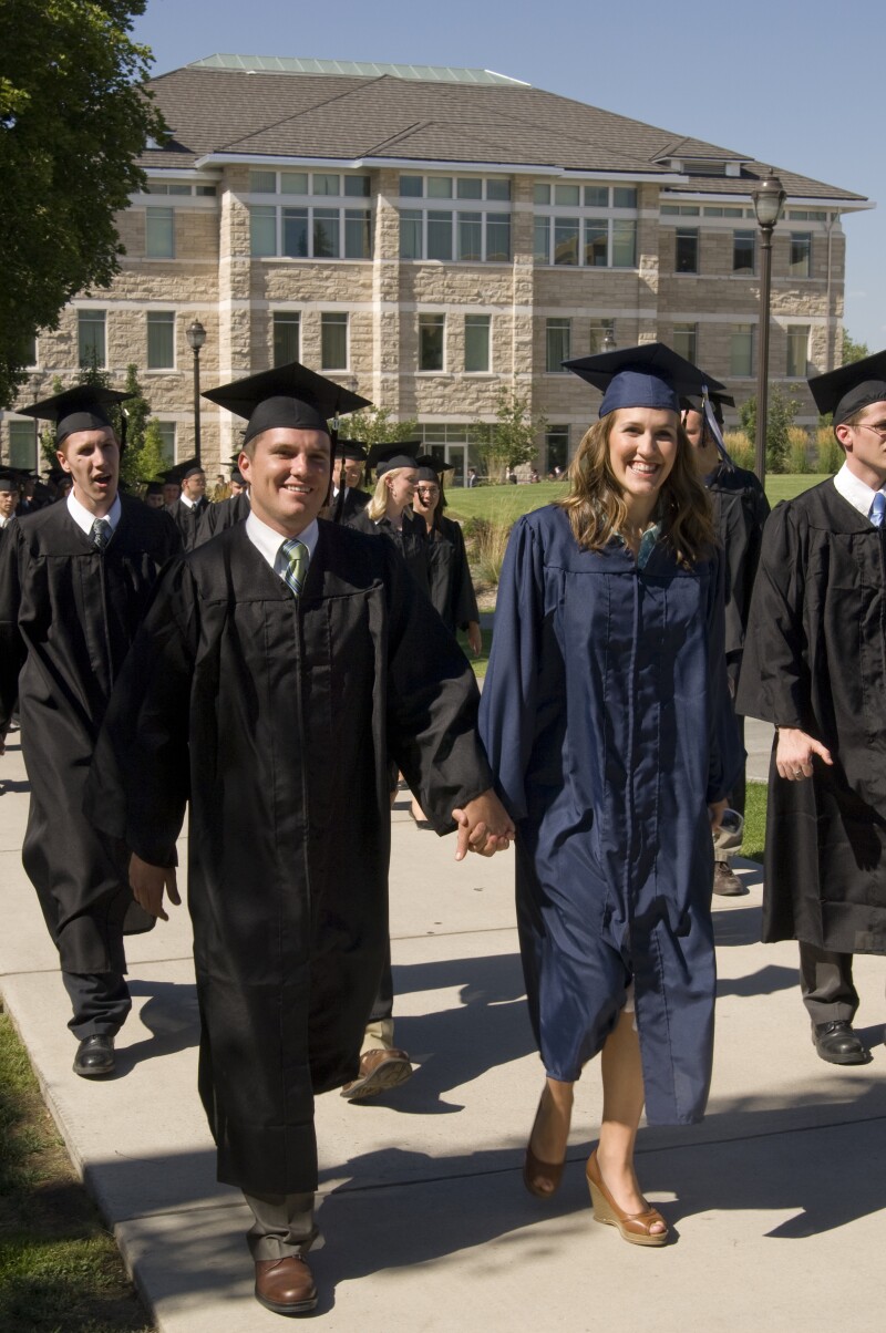 BYU-Idaho graduates smiling and walking on campus in front of the Spori building