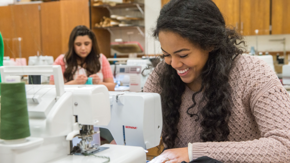 An apparel entrepreneurship student smiles over a sewing machine