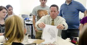 Students gather around their professor as he shows them a technique for illustration.