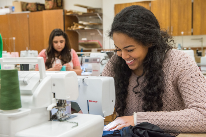 An apparel entrepreneurship student smiles over a sewing machine