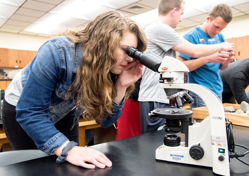 A student at a geology lab examines a sample with a microscope