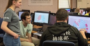 Three BYU-Idaho students look at family history group charts on computers during an I-Serve family history service event.