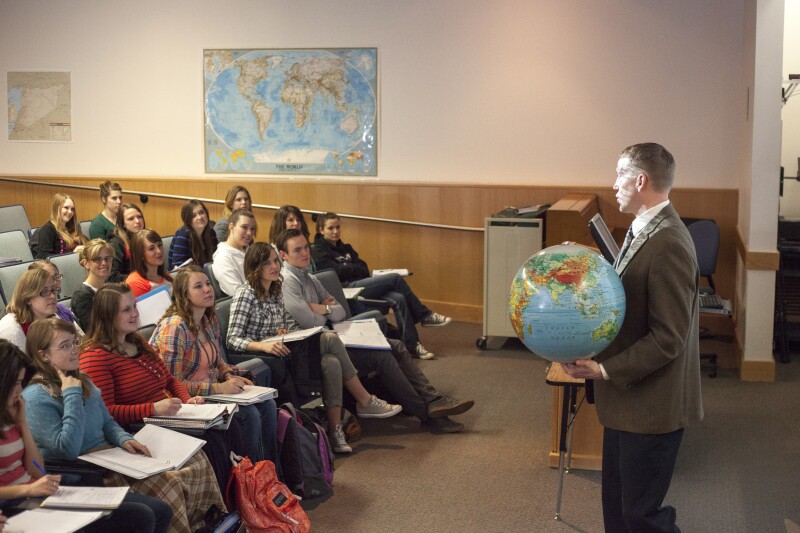 Brother Michael Madsen teaches his early morning Geography For Elementary Teachers class in the Ricks Building with a class sitting, listening to him