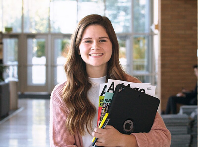 A Public Relations student holds her written work and smiles.