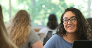 Female student smiling and looking at someone else while sitting at a desk with a computer