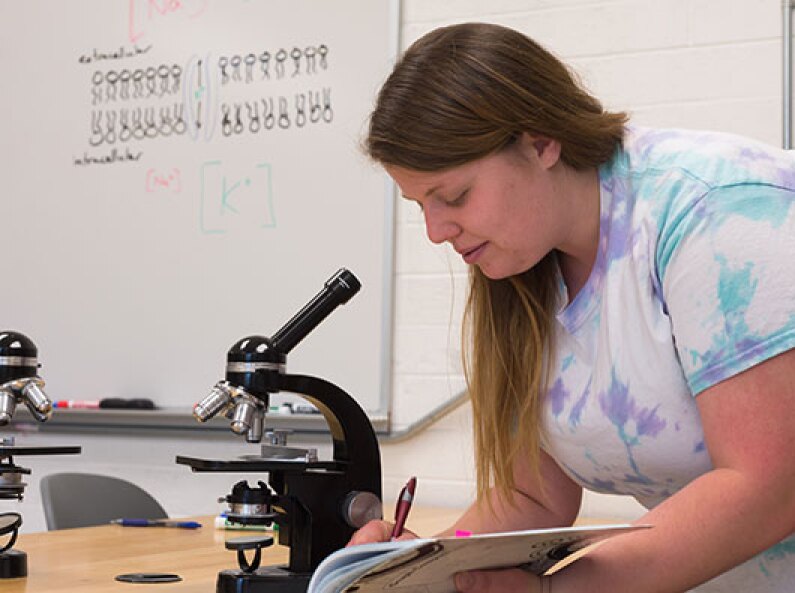 Biology student taking notes on a slide in a microscope