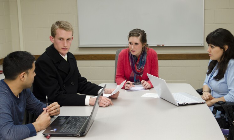 Four students sit at a table and discuss public administration policy making processes in a history class.