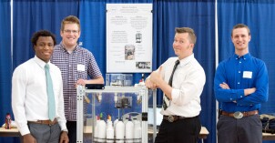 Four male students pose next to their creative project at there 2018 Research and Creative Works Conference.