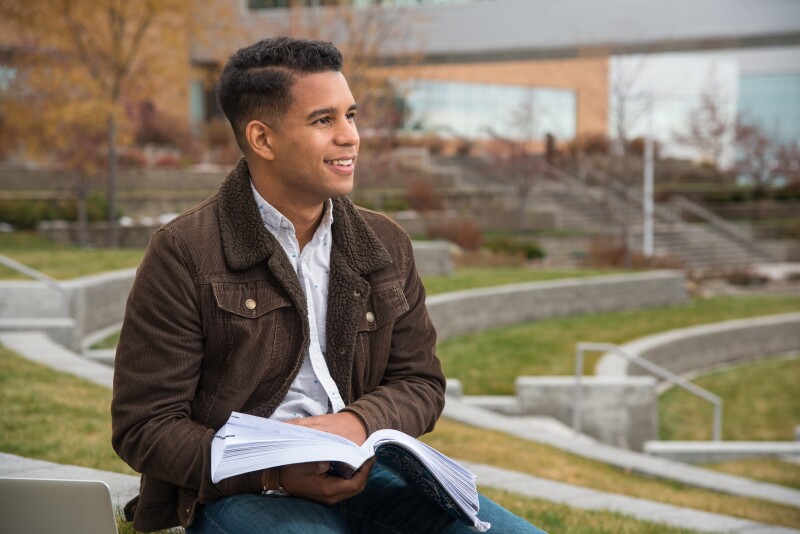 Student sitting outside on the BYU-Idaho campus, reading a book