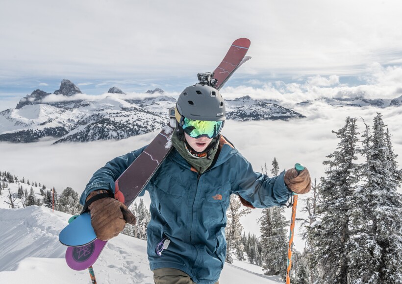 A skier with his skiis on his shoulder hiking up a mountain
