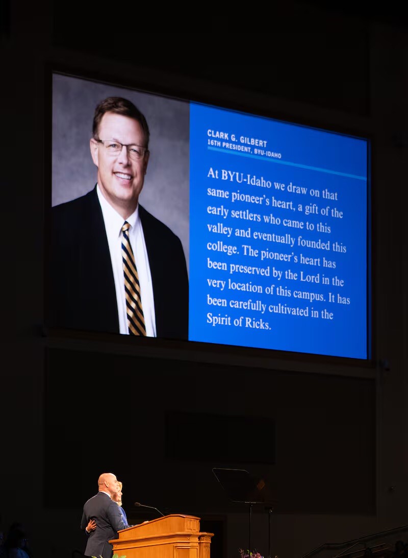 President Alvin F. Meredith III and Sister Jennifer Meredith speak at the Fall 2025 semester-opening devotional held in the BYU-Idaho Center on Sept. 16, 2025, in Rexburg, Idaho. A quote by Elder Clark G. Gilbert, General Authority Seventy and commissioner of Church education—as well as the 16th president of BYU–Idaho—is featured on the screen above the Merediths.