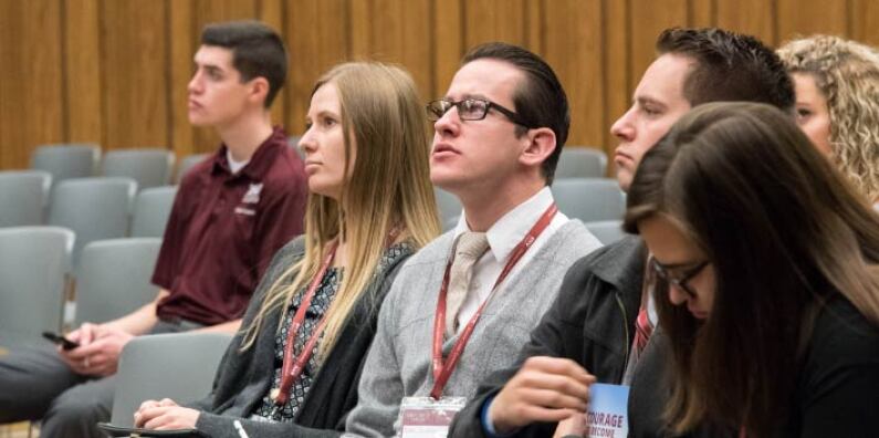 Several students listen to a speaker and take notes.