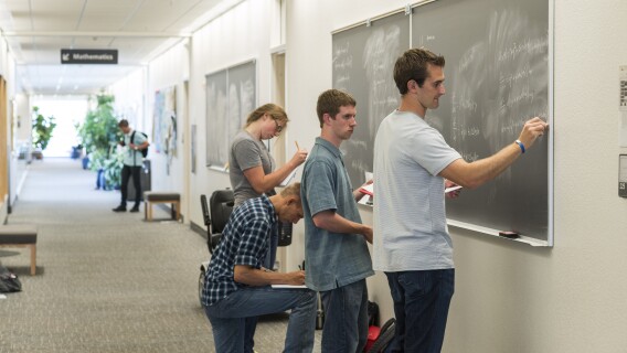 Students solve math equations on a chalkboard.