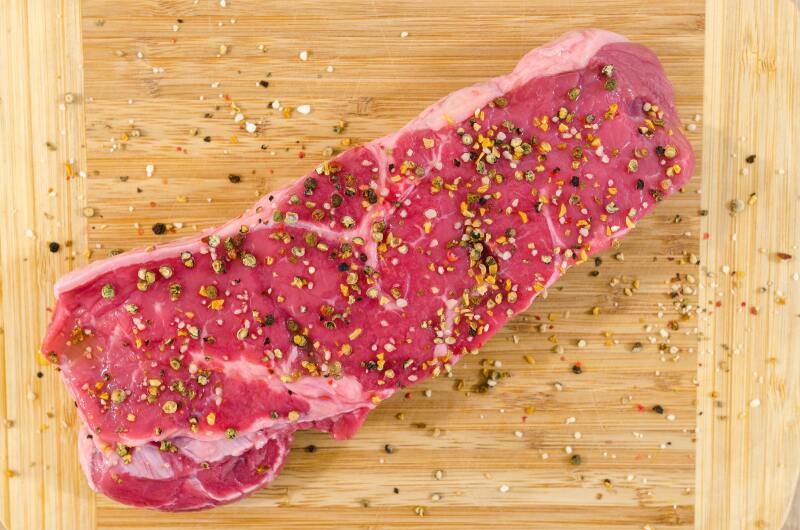 Cut of beef on a cutting board with seasoning