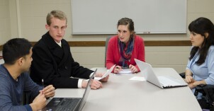 Four students sit at a table and discuss policy making processes in a public administrations class