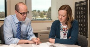 Male teacher mentoring a female student with a book a pencil.
