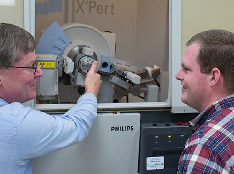 A professor shows and explains a piece of machinery to a student.