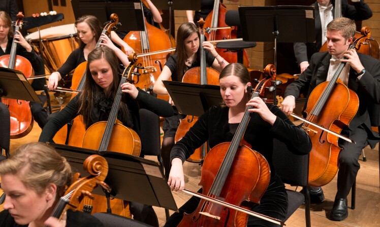 Students play cellos in a symphony orchestra.