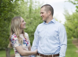 A married couple smiling at each other in a green field with trees