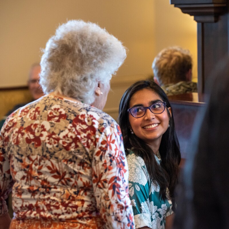 A female BYU-Idaho student smiles while talking with an elderly woman at a local nursing home during a student life activity.