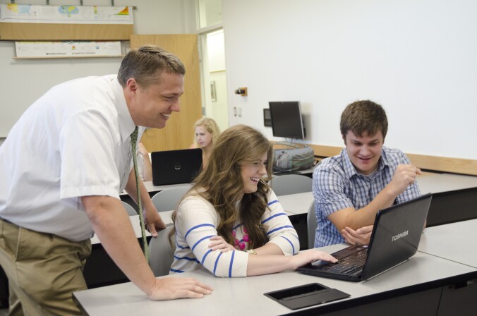 Two students smile while viewing a computer with a faculty member in a social studies education history class