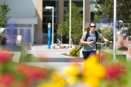 A female student walks her bicycle on a sidewalk at the BYU-Idaho campus,