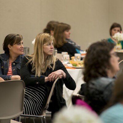 Women sitting around tables listening to a speaker at the Women's Luncheon.