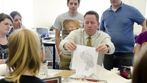 Students gather around their professor as he shows them a technique for illustration.