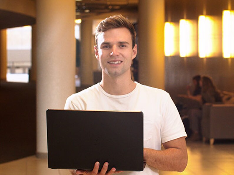 A Digital and Social Media student sits in the I-Center on their computer and smiles.