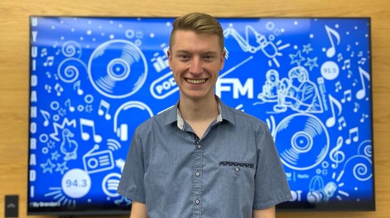 Chad Bell poses in front of a monitor displaying radio art