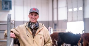 A male student stands in front of cattle and smiles at the Livestock Center.