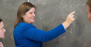 teacher showing students a math problem on the chalkboard