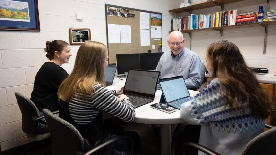 Economic students gather around a professor's desk as he teaches them