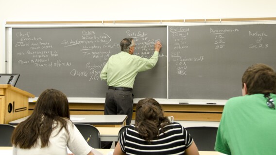 History Professor Bob Inama writes on a chalkboard while teaching his American Government class