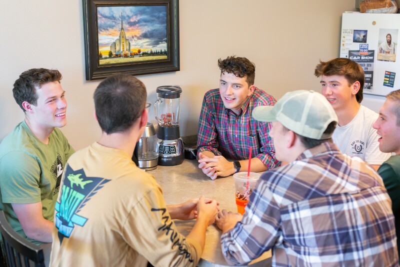 Male roommates sitting around the kitchen table talking to one another.