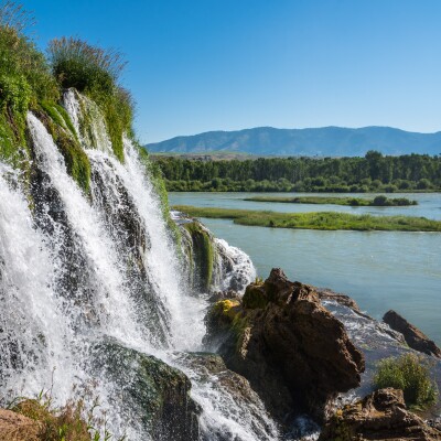 Rushing waterfalls at Fall Creek with a lake, trees, and mountains in the background.