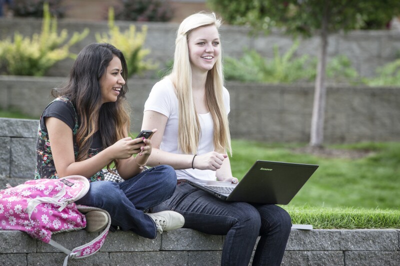 Two female students sit in the yard by the Ampitheater on the first day of classes. 