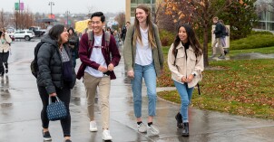 A group of BYU-Idaho students smiling and walking on campus towards the Manwaring Center on a rainy day.