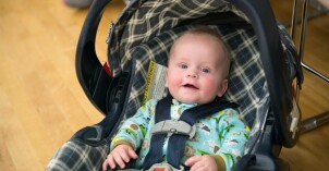 A baby sitting in a car seat, smiling at the camera