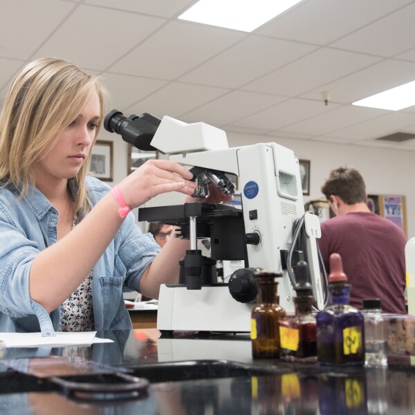 Student changing objectives on a microscope to increase magnification.