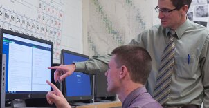 A professor helps a student understand a concept on the computer.