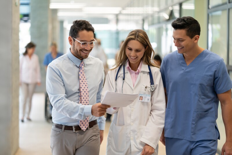 Male supervisor of a hospital showing some paperwork to female doctor and nurse while walking down the corridor all smiling