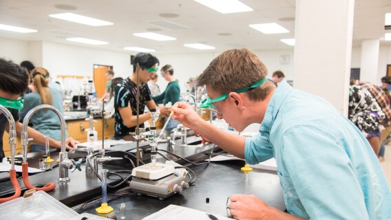 Student in protective gear pipes solution into a vial using a pipette.