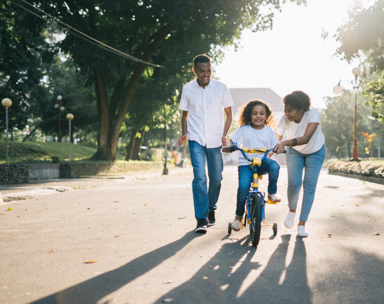 Two parents teaching their daughter how to ride a bike.