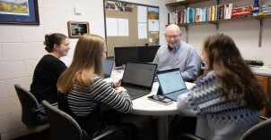 Economic students gather around a professor's desk as he teaches them