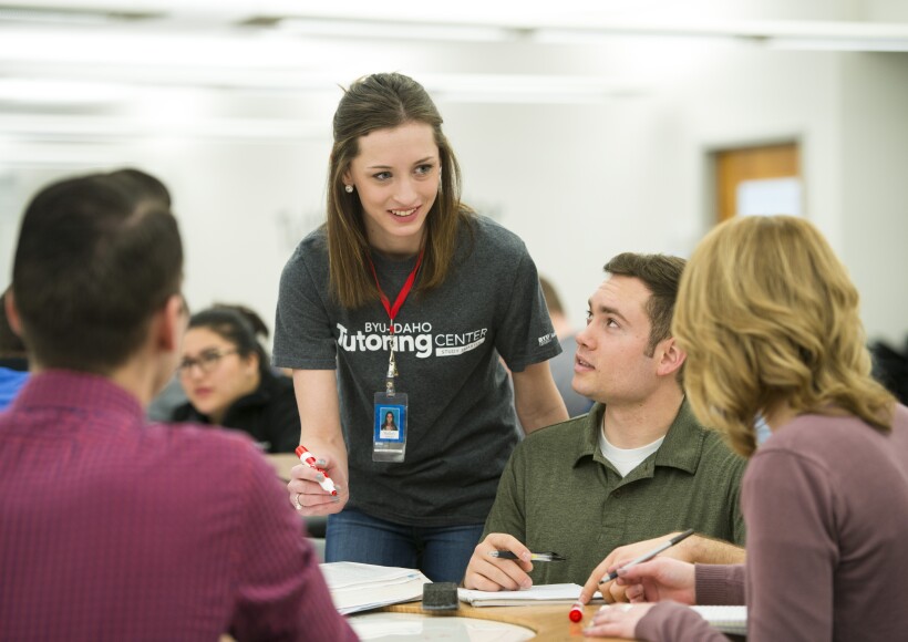 A female student tutor helps three students with class questions at the Tutoring Center.
